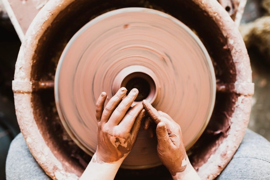 A potter's hands centering a small mound of clay on a spinning wheel head, seen from above