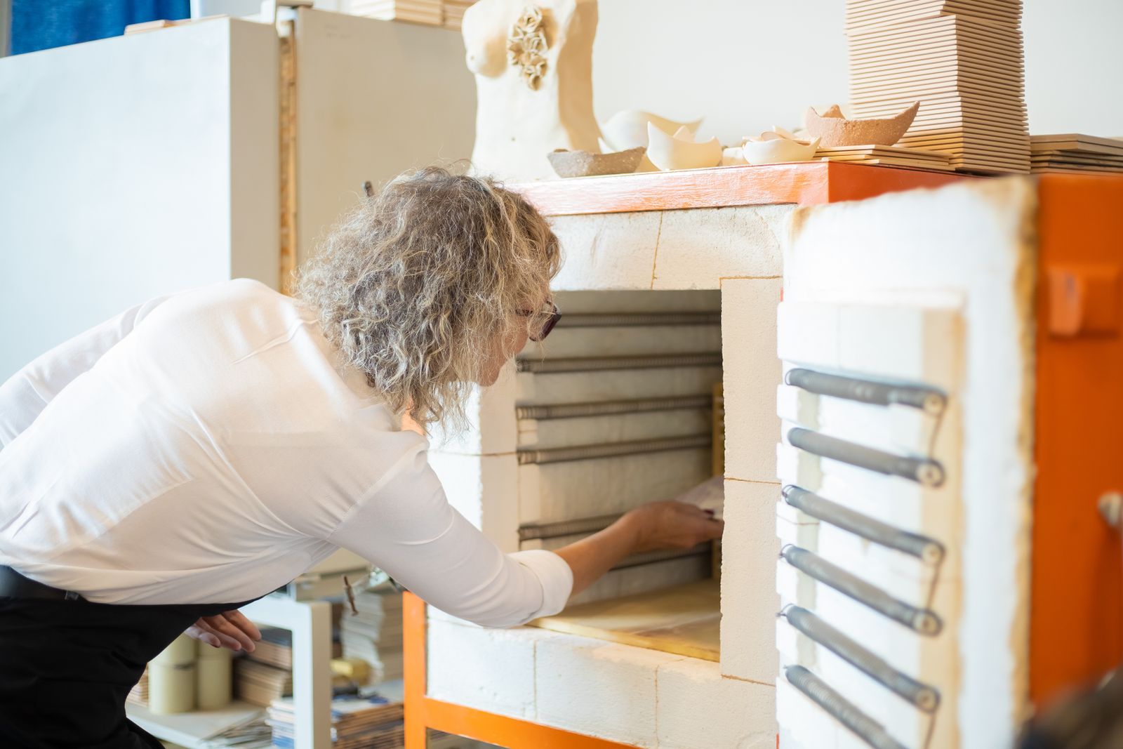 Potter loading bisque-fired ceramic pieces into a top-loading electric kiln before a glaze firing