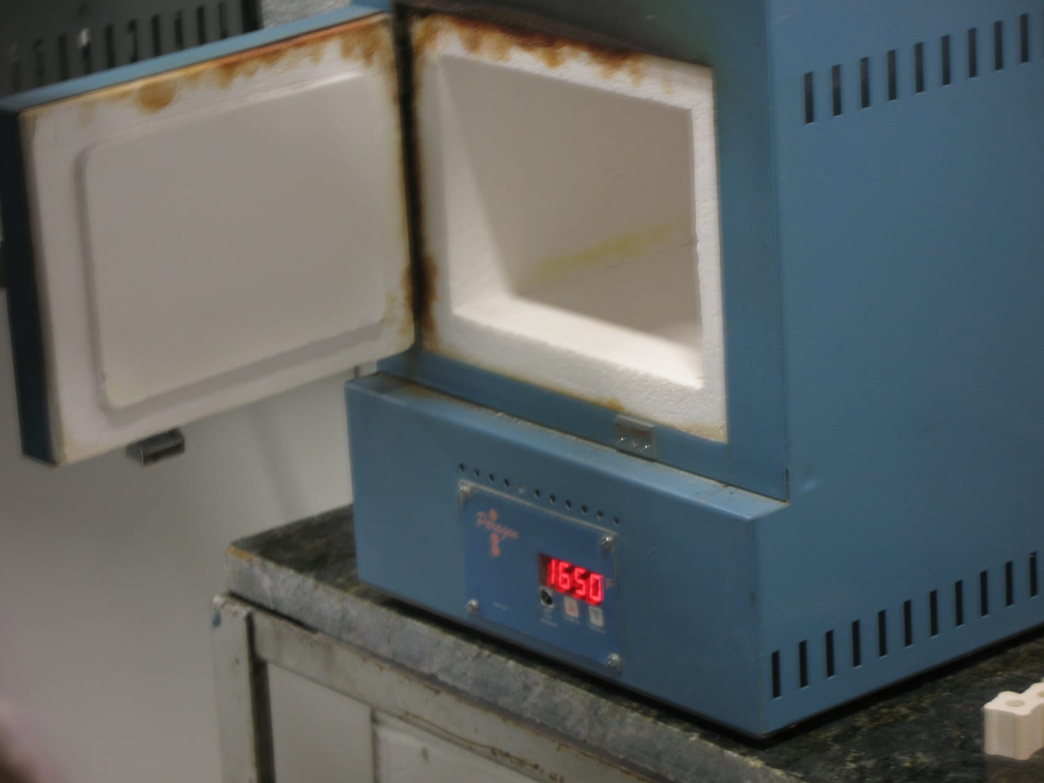 A small front-loading Paragon electric kiln with its door open, controller showing 1650F