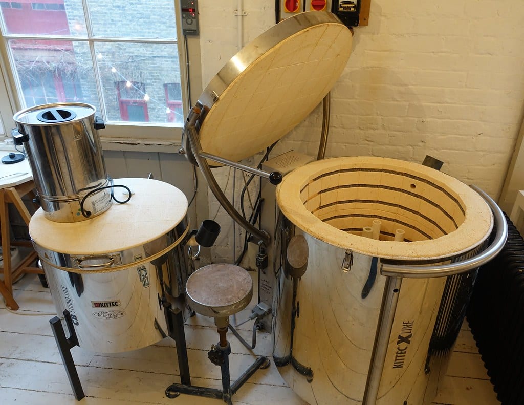 Electric top-loading kilns in a studio, one with the lid raised