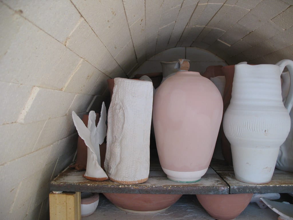 Greenware pieces and a sculpture sitting on a kiln shelf with posts inside the chamber