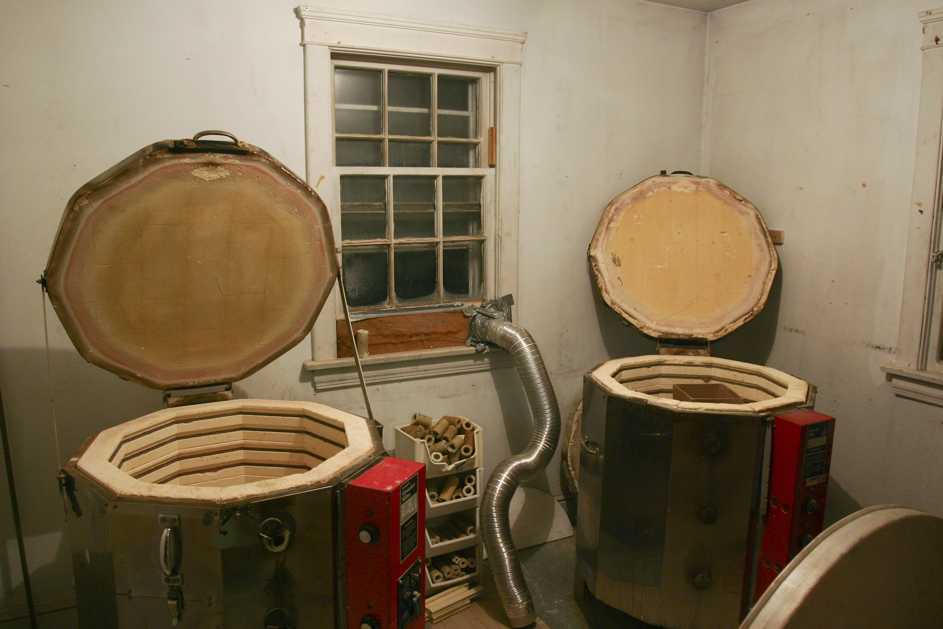 Two top-loading electric pottery kilns standing side by side in a home ceramics studio