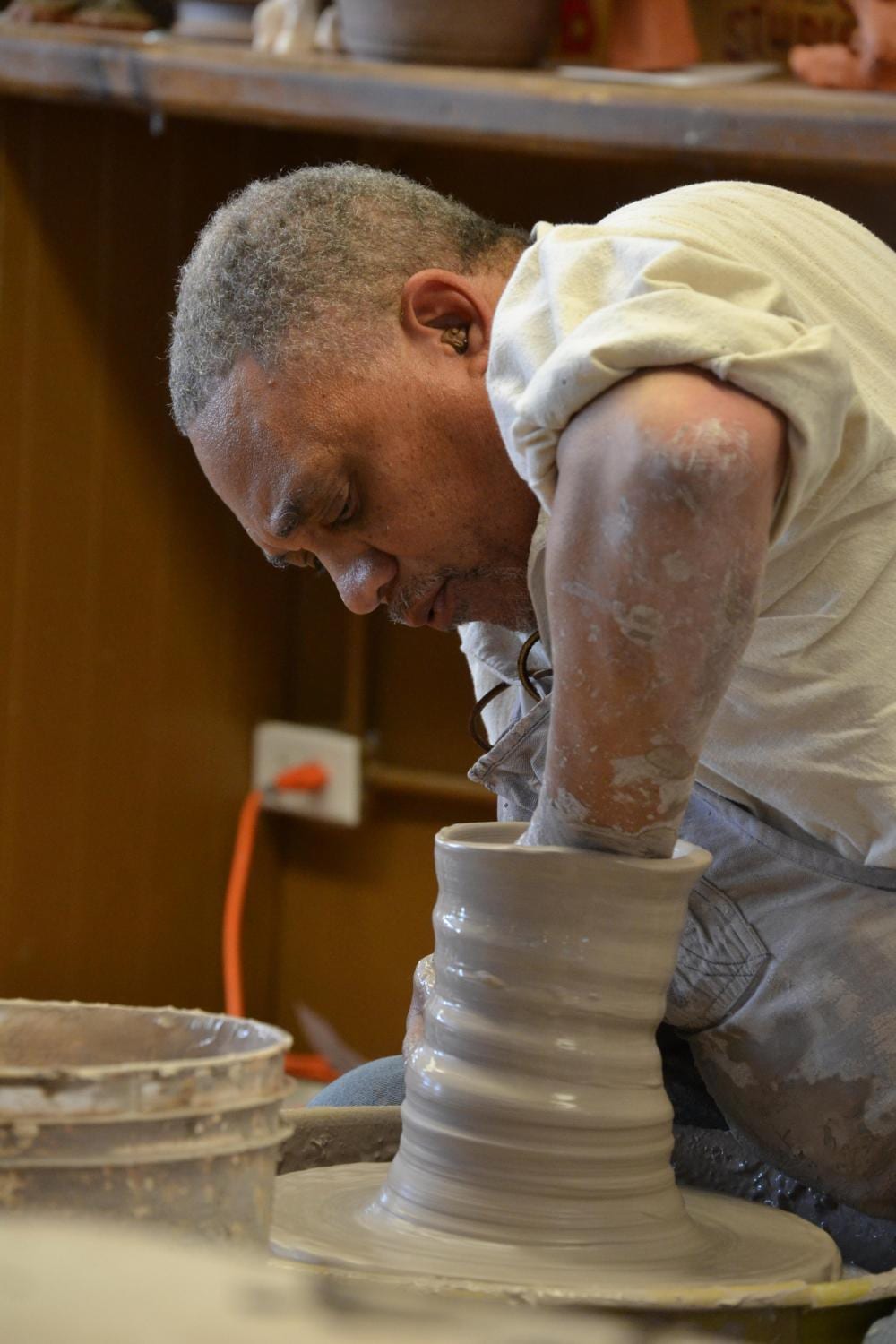 A potter throwing a tall form on an electric pottery wheel