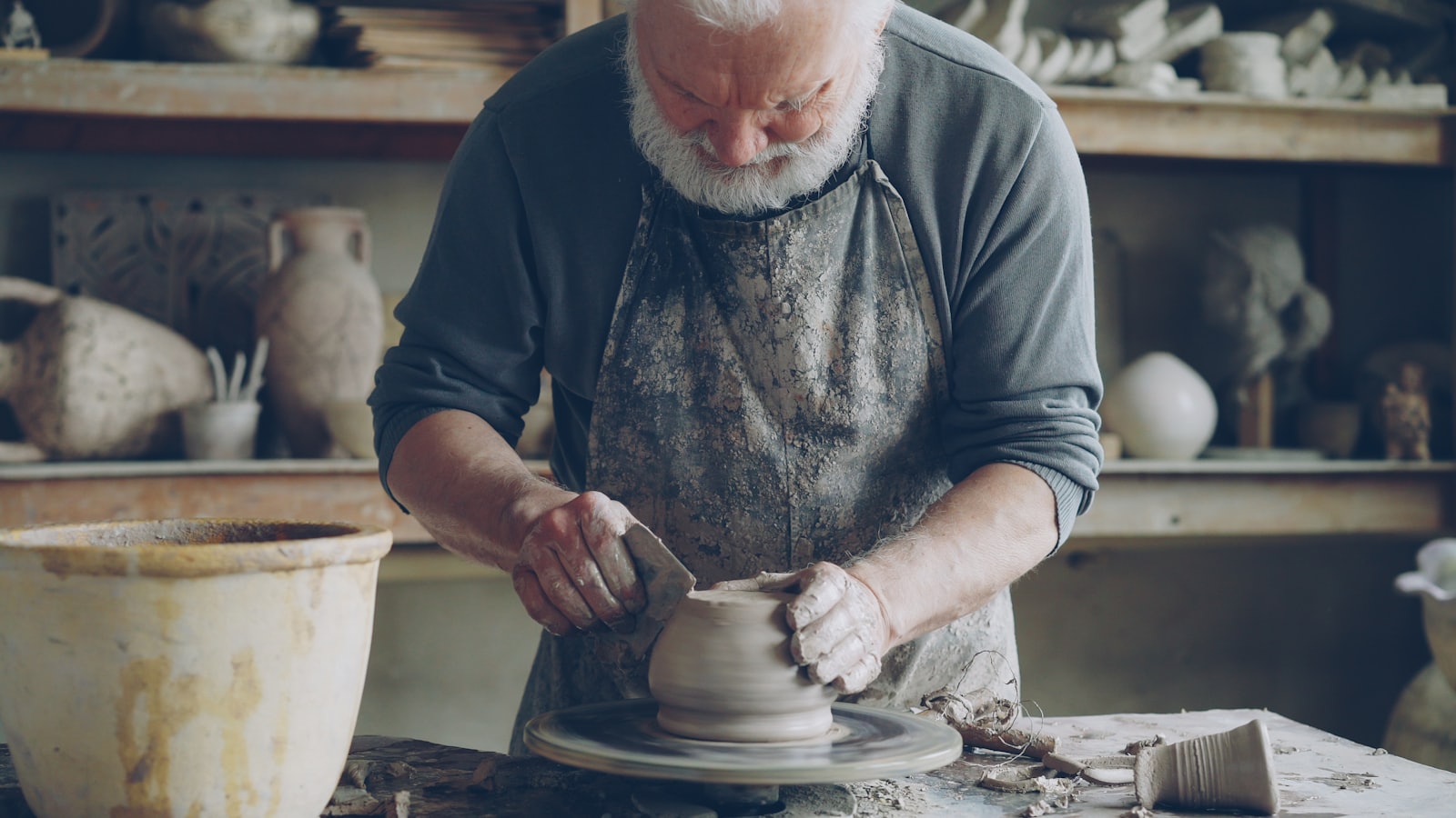 Potter's hands shaping a tall clay vessel on a floor pottery wheel