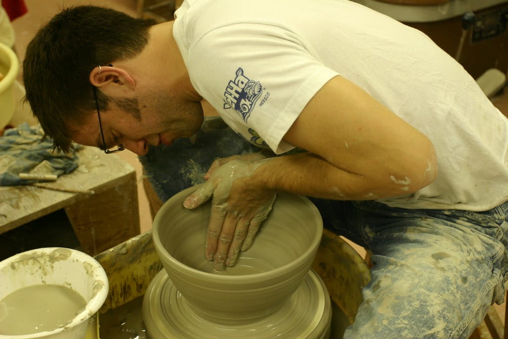 A potter opening a wide bowl on the wheel, both hands inside the spinning clay