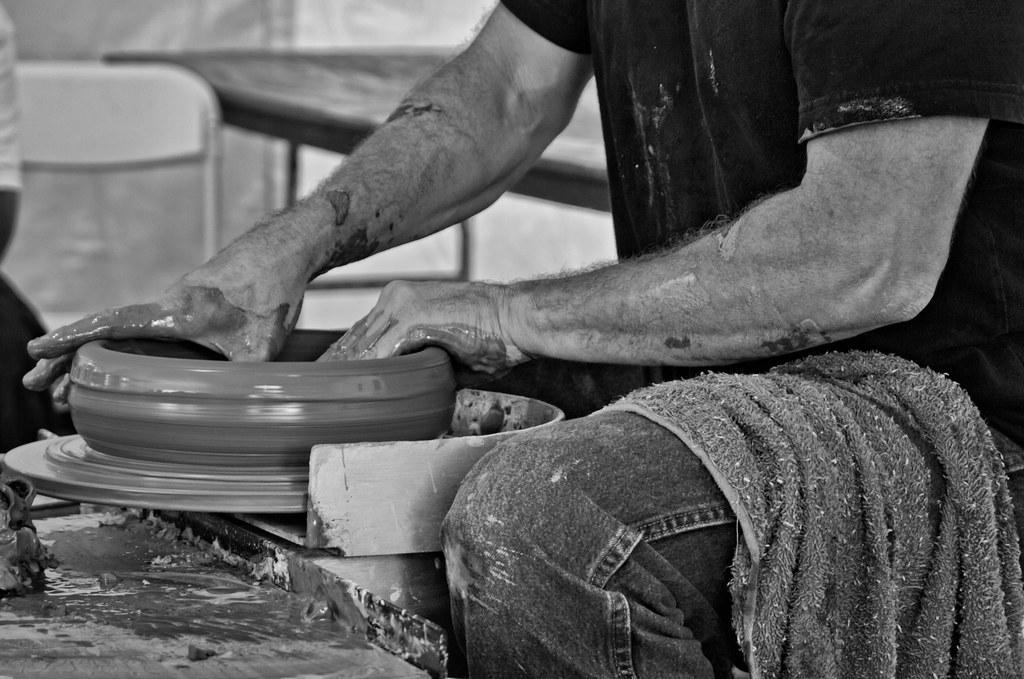 A potter's hands opening a centered lump of clay and beginning to pull the walls upward
