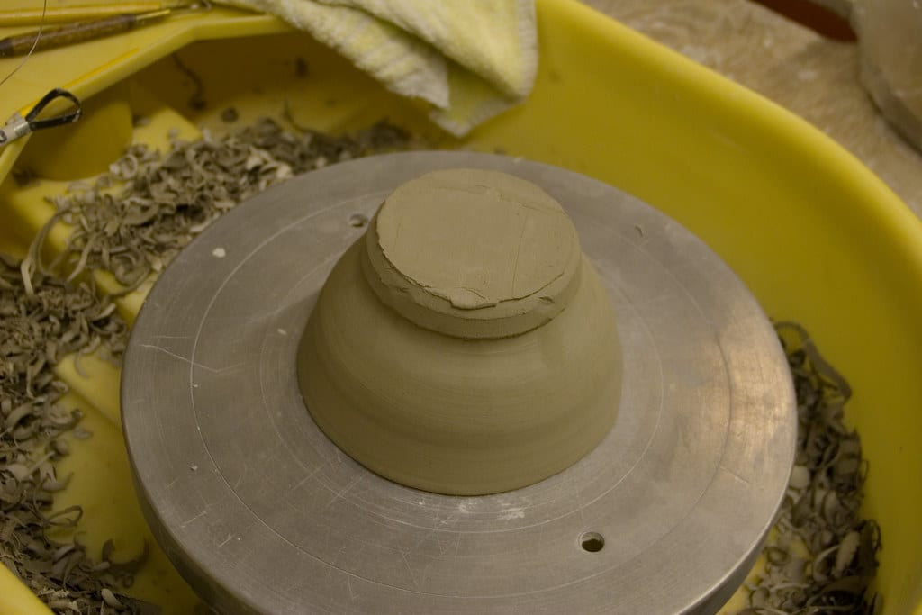 Trimming an inverted bowl on the wheel head, clay shavings collecting in the splash pan