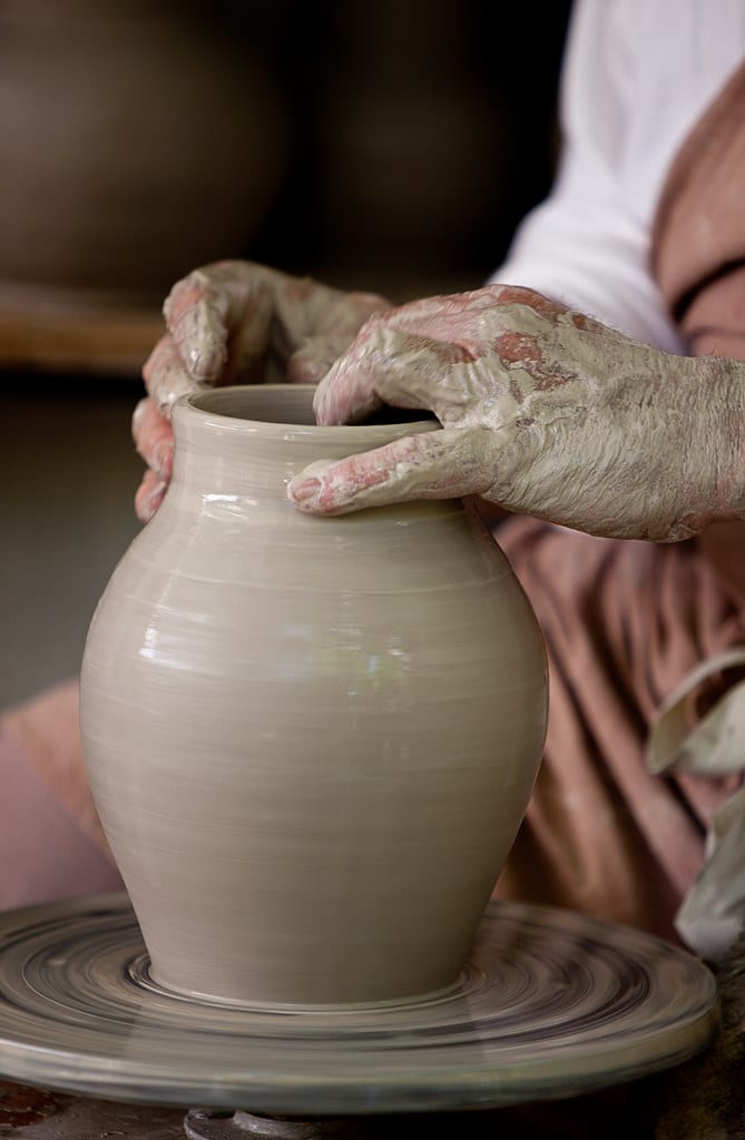 Close-up of a potter's hands shaping the wall of a pot on a spinning wheel
