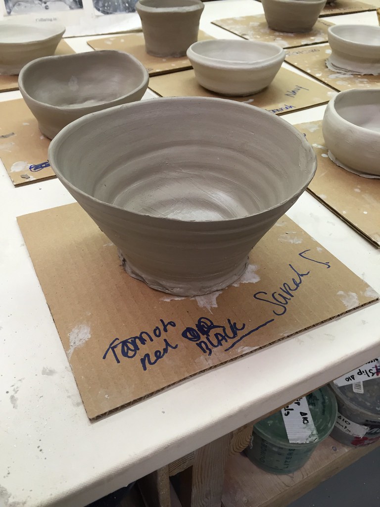 Potter pulling up clay walls on a wheel to form a cylinder